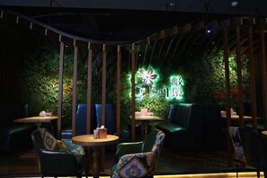 Un restaurant à la lumière tamisée, avec des sièges verts, un panneau néon et une structure de plafond en bois.