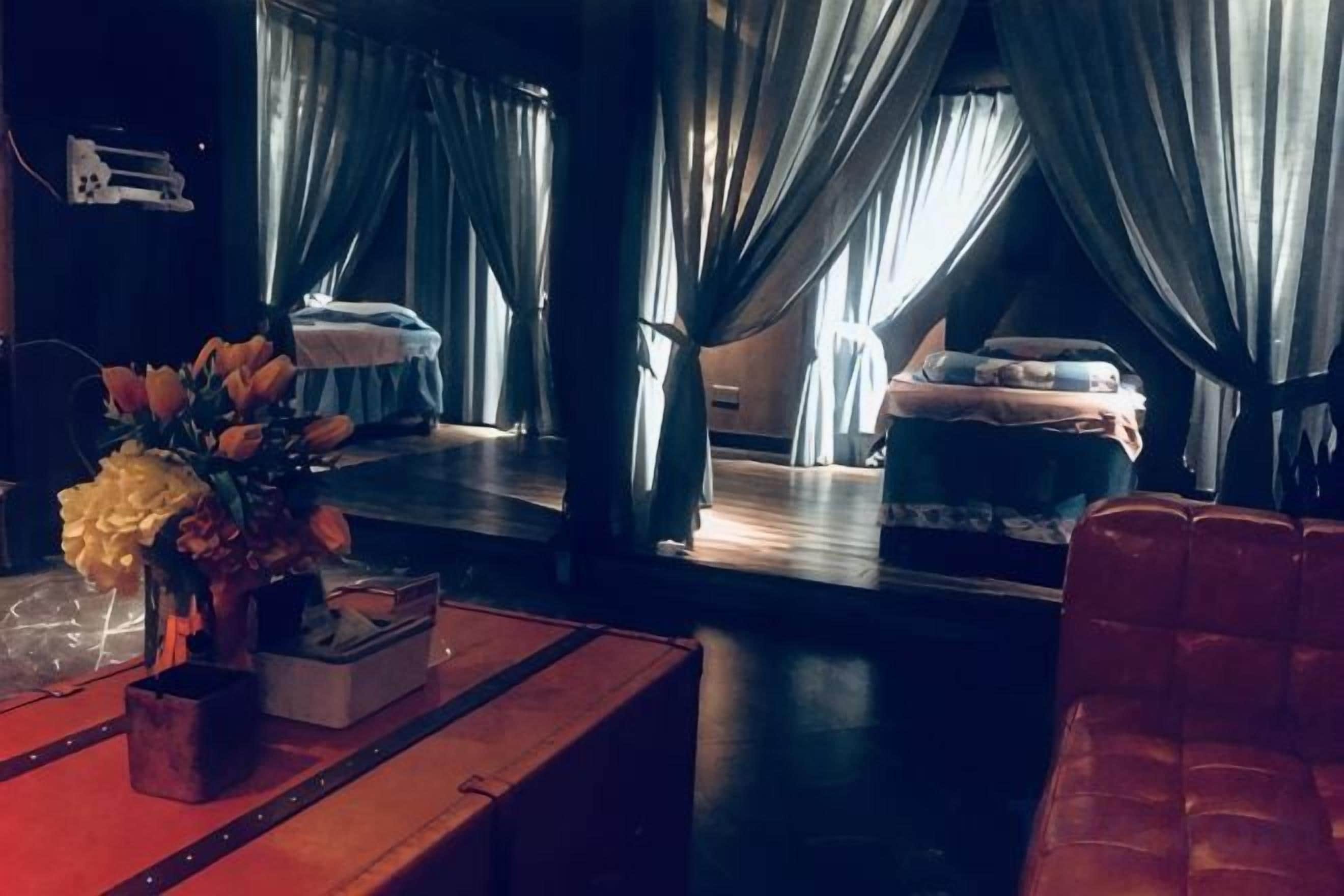 A room with a bed, a red chair, a wooden table with a vase of flowers, and curtains.
