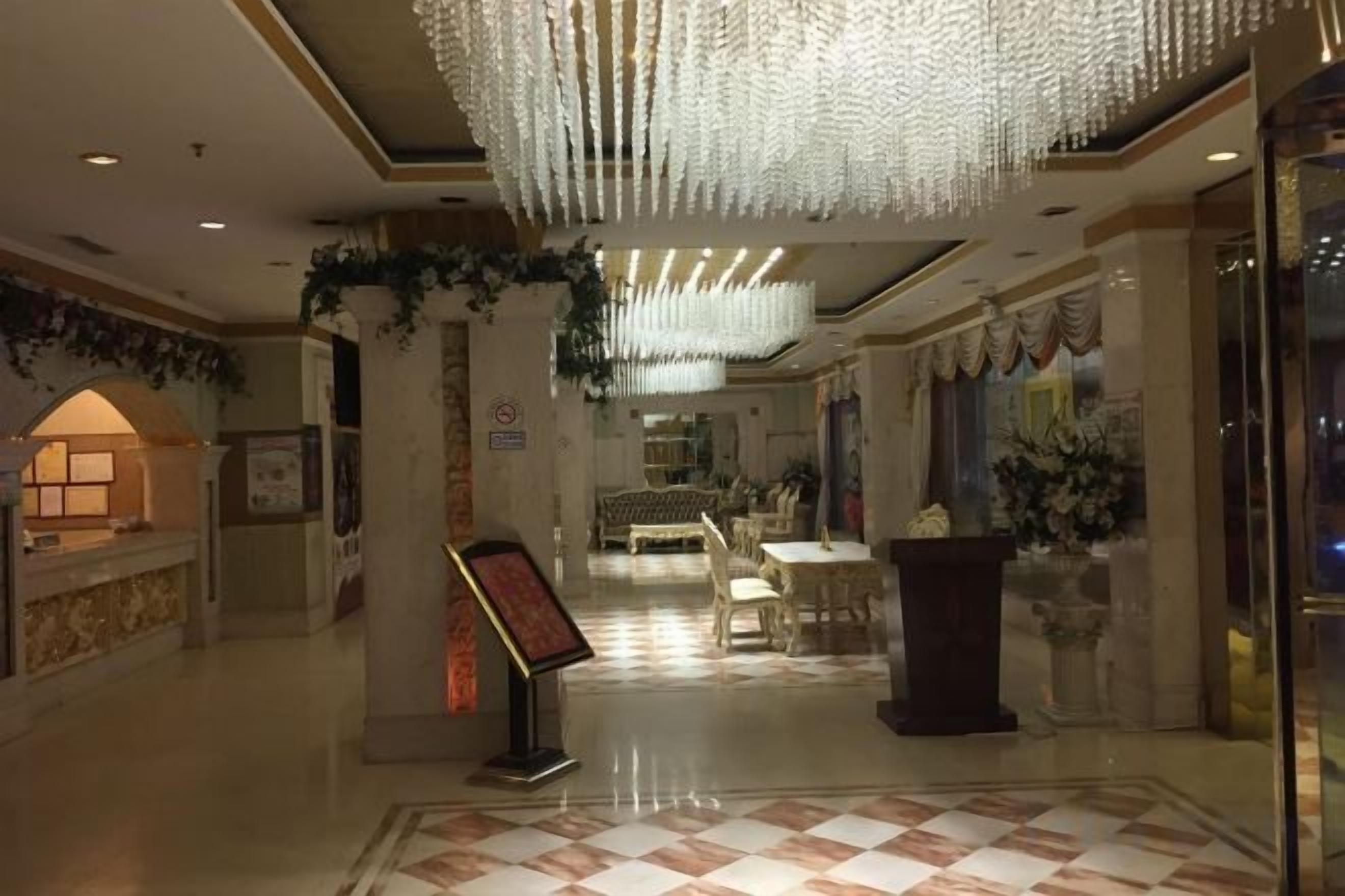 A hotel lobby with a check-in counter, a reception desk, a seating area, and a chandelier.