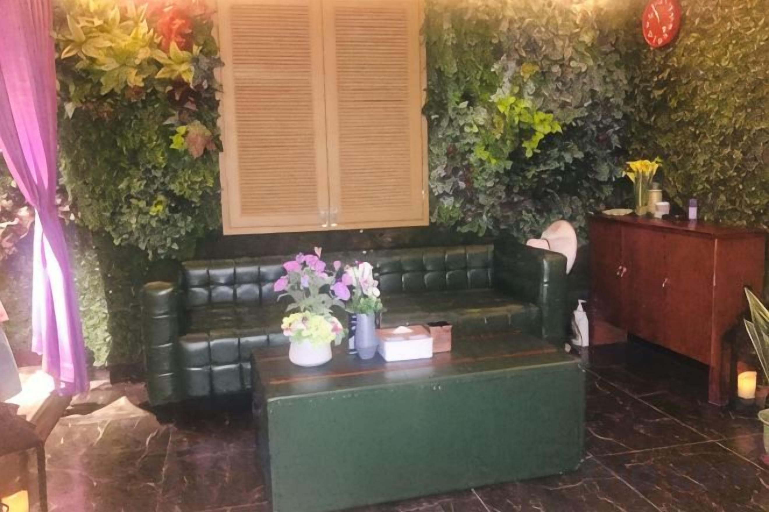 A green sofa, a small table with flowers, and a wooden cabinet in a room with a green wall and a clock.