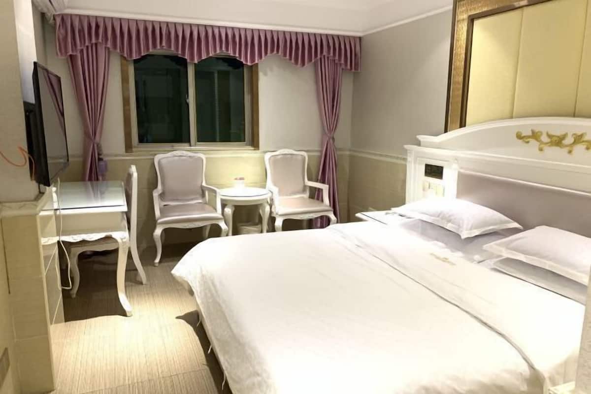 Habitación de hotel con una cama grande, un escritorio con una silla, un televisor y dos sillas.