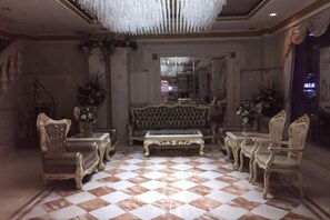 Un hall d’entrée avec un sol à carreaux, des canapés richement décorés et un lustre.