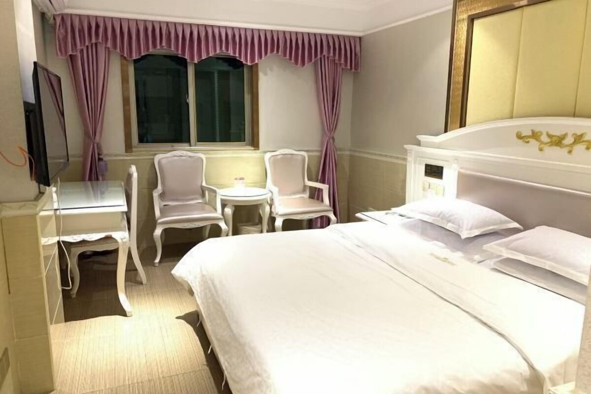 Een hotelkamer met een bed, twee stoelen, een bureau, een televisie en een raam met gordijnen.