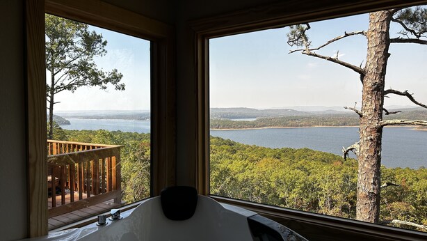 Una habitación con un gran ventanal que ofrece vistas a un lago, una terraza y una bañera de hidromasaje.