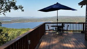 Una terraza de madera con mesa y sillas, una sombrilla y vistas a un lago y montañas.