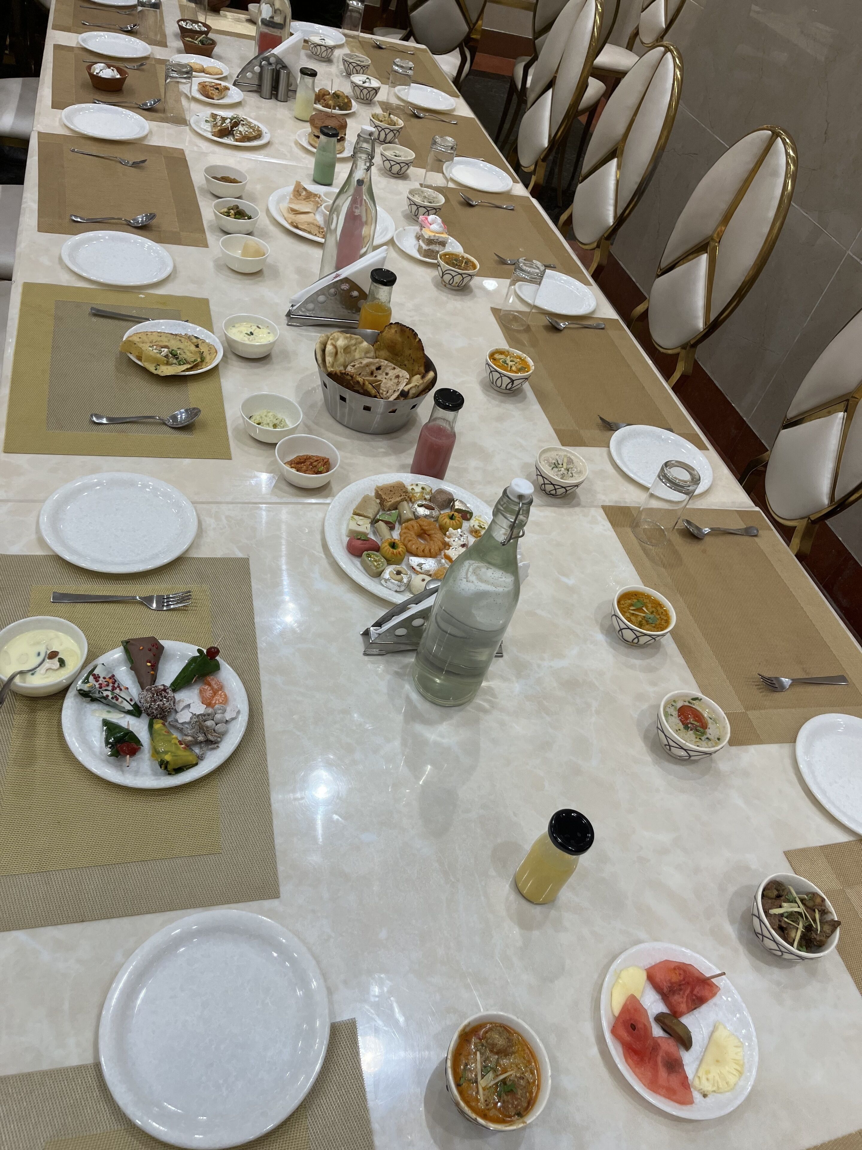 Una larga mesa de comedor dispuesta con diversos platos, incluyendo fuentes de comida, tazones y botellas, probablemente en un comedor de hotel.