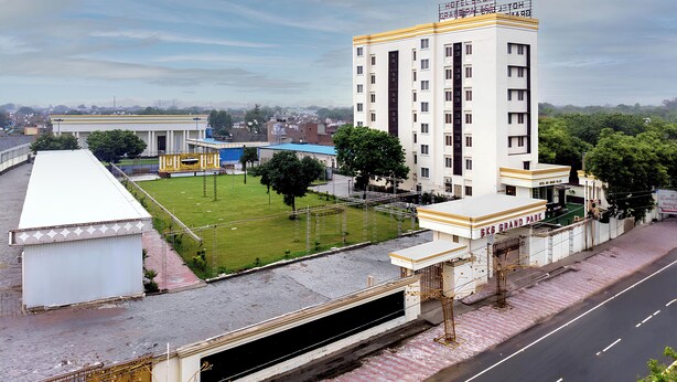 Un hotel de varios pisos con techo plano, zona de estacionamiento y césped verde.