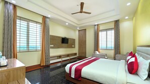 Una habitación de hotel con cama, escritorio, televisión y ventana con cortinas.