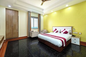 Habitación de hotel con una cama grande, un armario, una zona de estar y una ventana con cortinas.