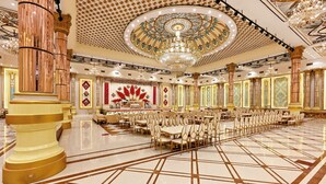 Un gran salón de banquetes con columnas ornamentales, una lámpara de araña grande y un techo con diseños.