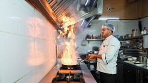 Un cocinero preparando comida con una llama grande sobre una estufa a gas en una cocina.