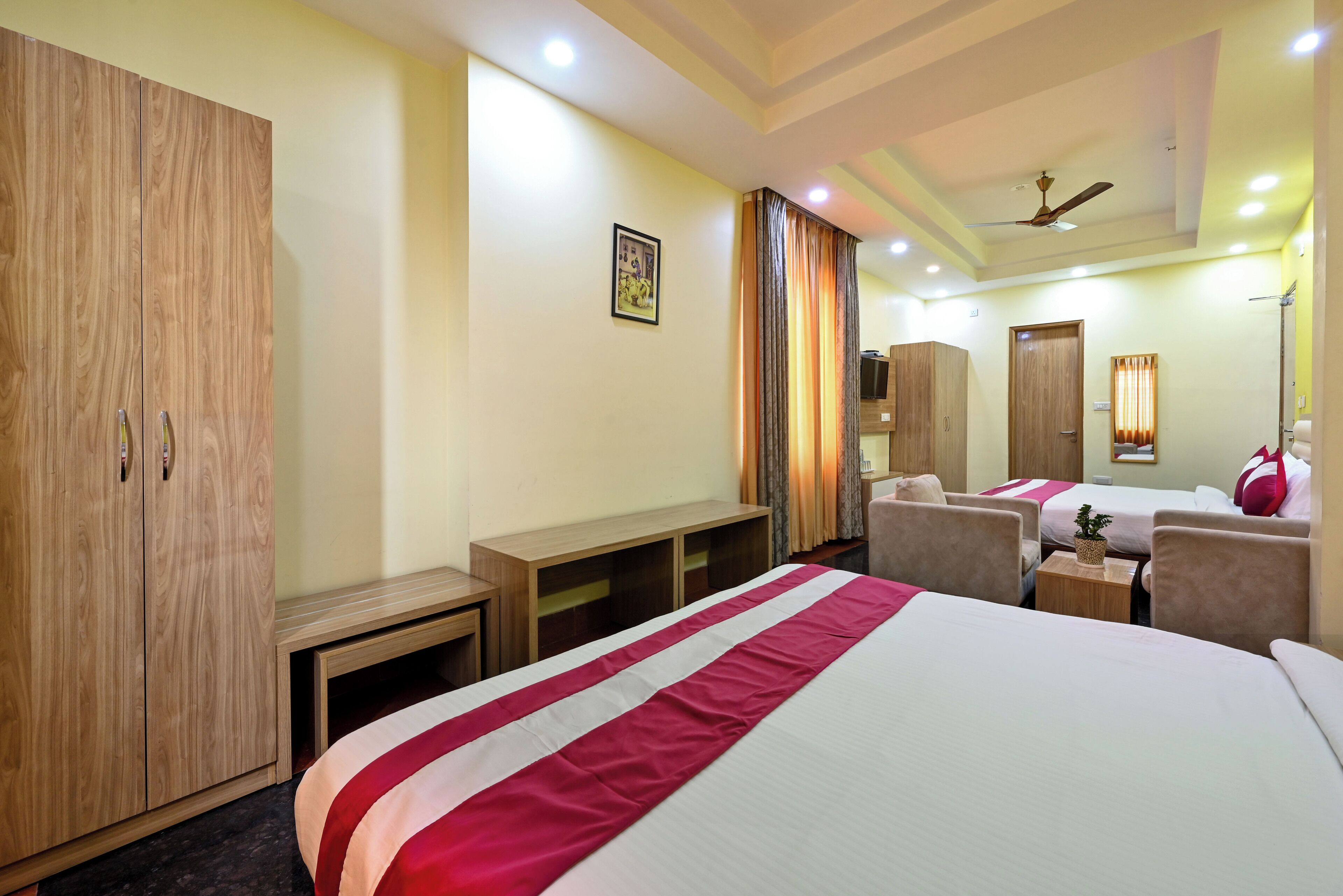 A hotel room with a large bed, a wardrobe, a desk, a chair, and a small table with a plant.