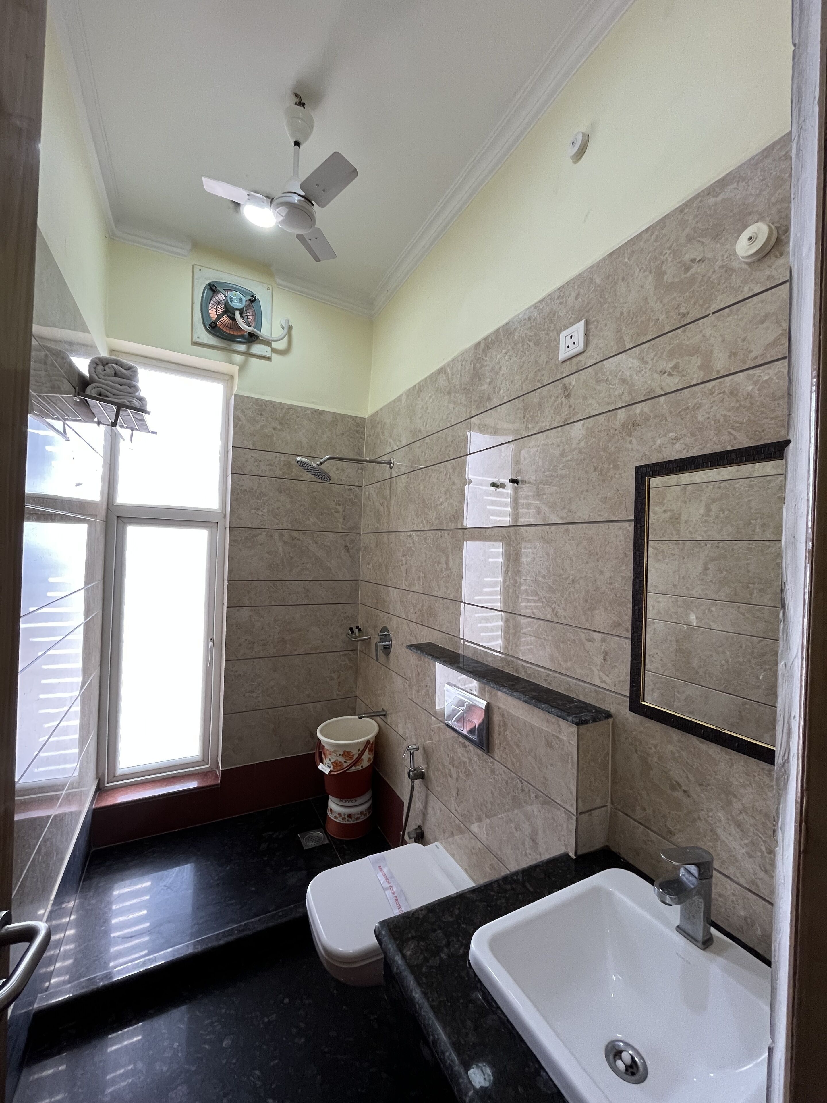 A bathroom with a toilet, sink, shower, and a ceiling fan.