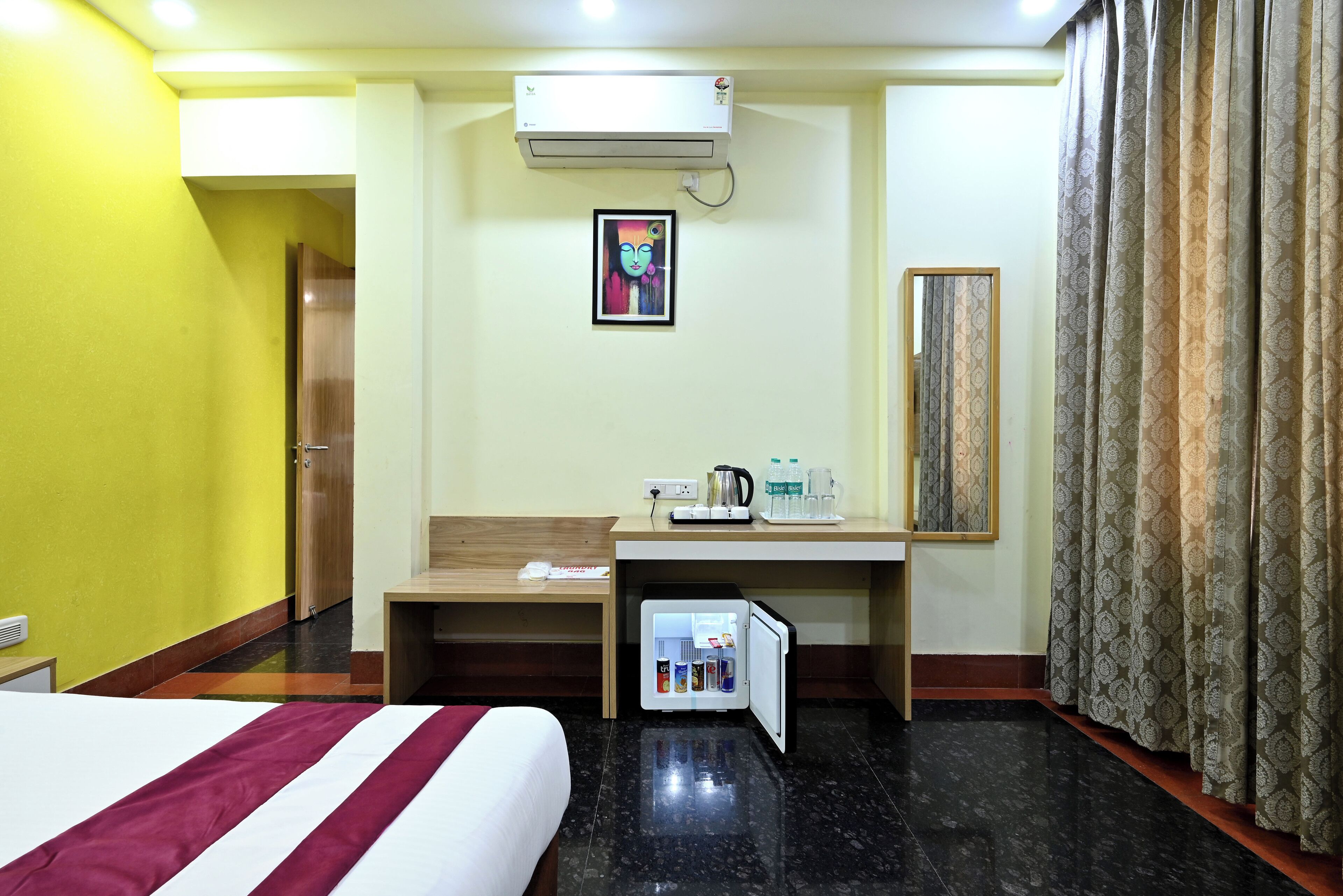 Une chambre d’hôtel avec un lit, un bureau doté d’un réfrigérateur, une machine à café et un tableau au mur.