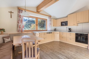 A kitchen with wooden cabinets, a dining table, and a cross on the wall. - Apartment "Hörbiger" with Mountain View, Balconies & Wi-Fi (Wildschönau)