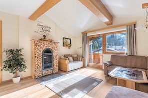 A cozy living room with a fireplace, a sofa, a table, and a large window. - Apartment "Hörbiger" with Mountain View, Balconies & Wi-Fi (Wildschönau)