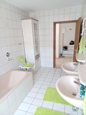 Une salle de bain avec une baignoire, deux lavabos, une douche, un porte-serviettes et un miroir.