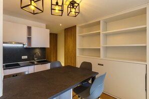 Een moderne keuken met een donker aanrechtblad, witte kasten en een ingebouwde oven. Er staan twee stoelen bij een kleine eettafel.
