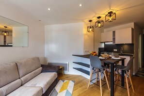 A modern apartment with a sofa, dining table, chairs, and a kitchen area.