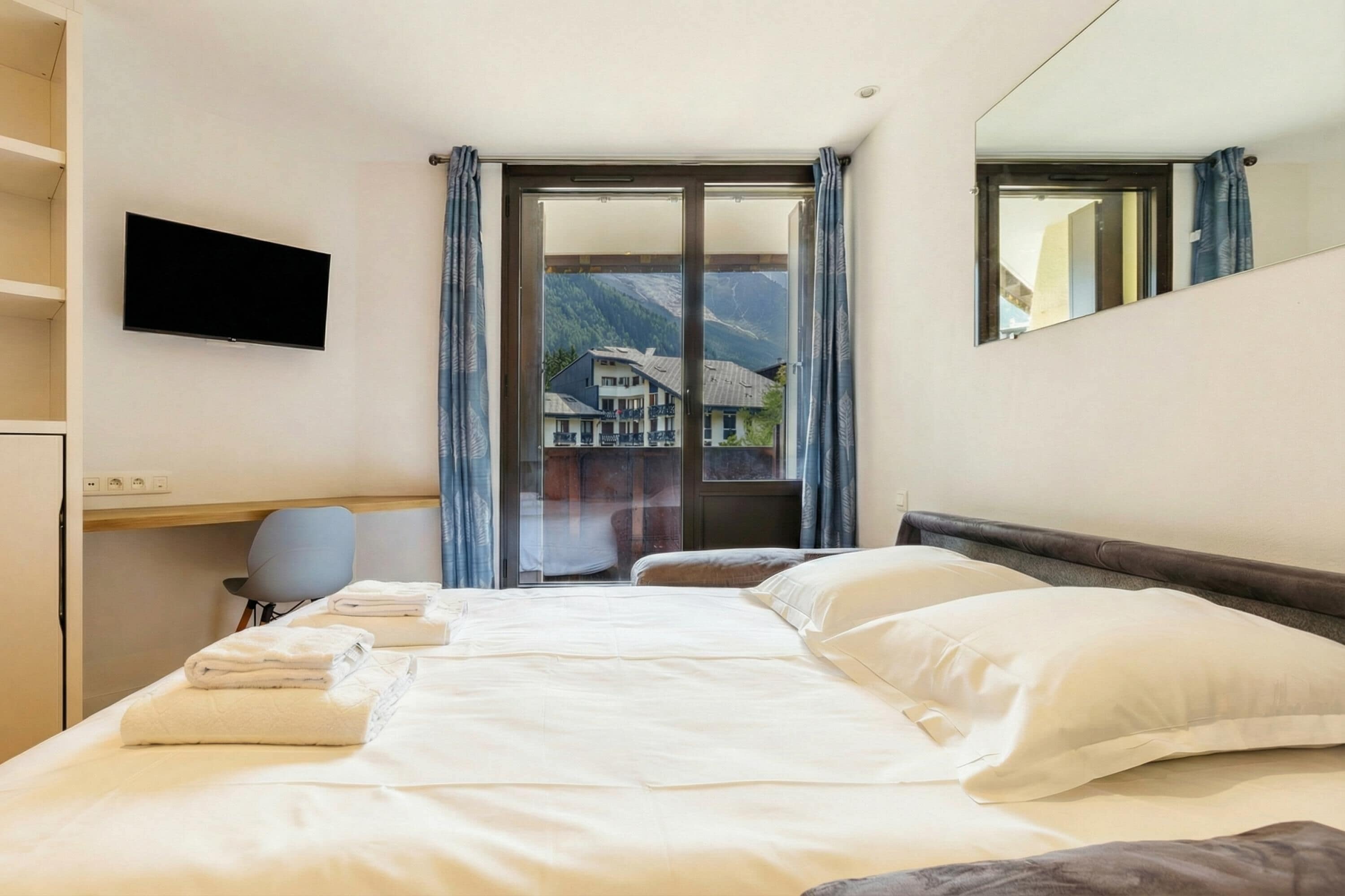 Ein Hotelzimmer mit einem großen Bett, einem wandmontierten Flachbildfernseher, einem Schreibtisch mit Stuhl und Bergblick aus dem Fenster.