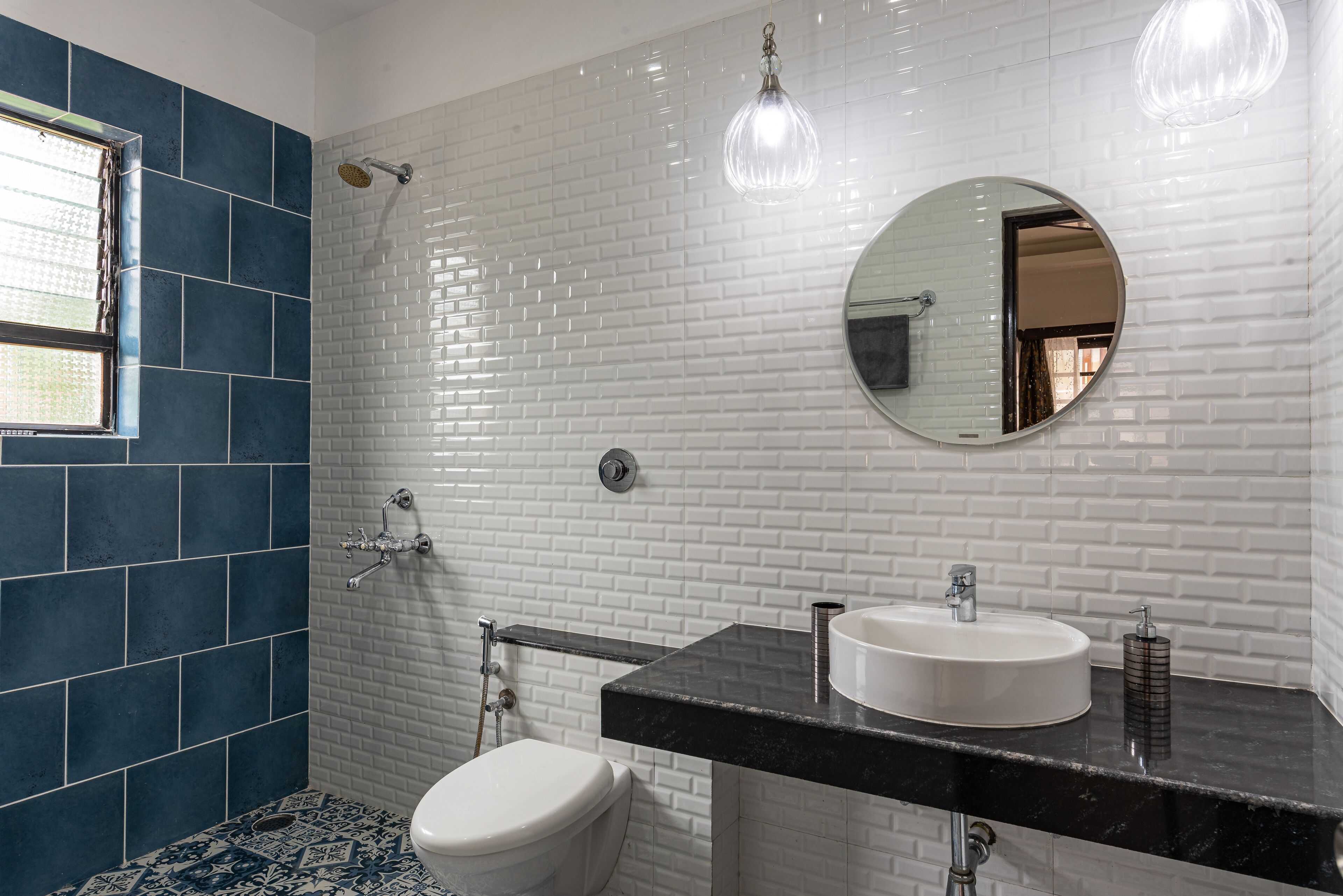 A bathroom with a white and blue tiled wall, a round mirror, a white sink, and a shower.