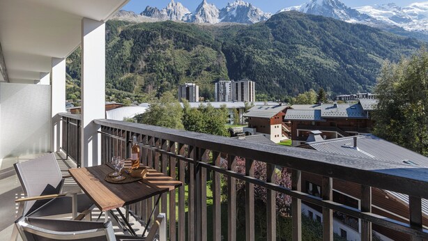A balcony with a table, chairs, and a bottle, overlooking a mountain landscape with buildings. - Résidence La Vallée Blanche in Chamonix Balcony & Mont Blanc Views, Chamonix, France (Chamonix)