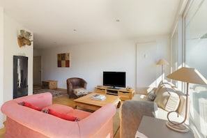 Een moderne woonkamer met een bank, fauteuil, salontafel en een flatscreen televisie.