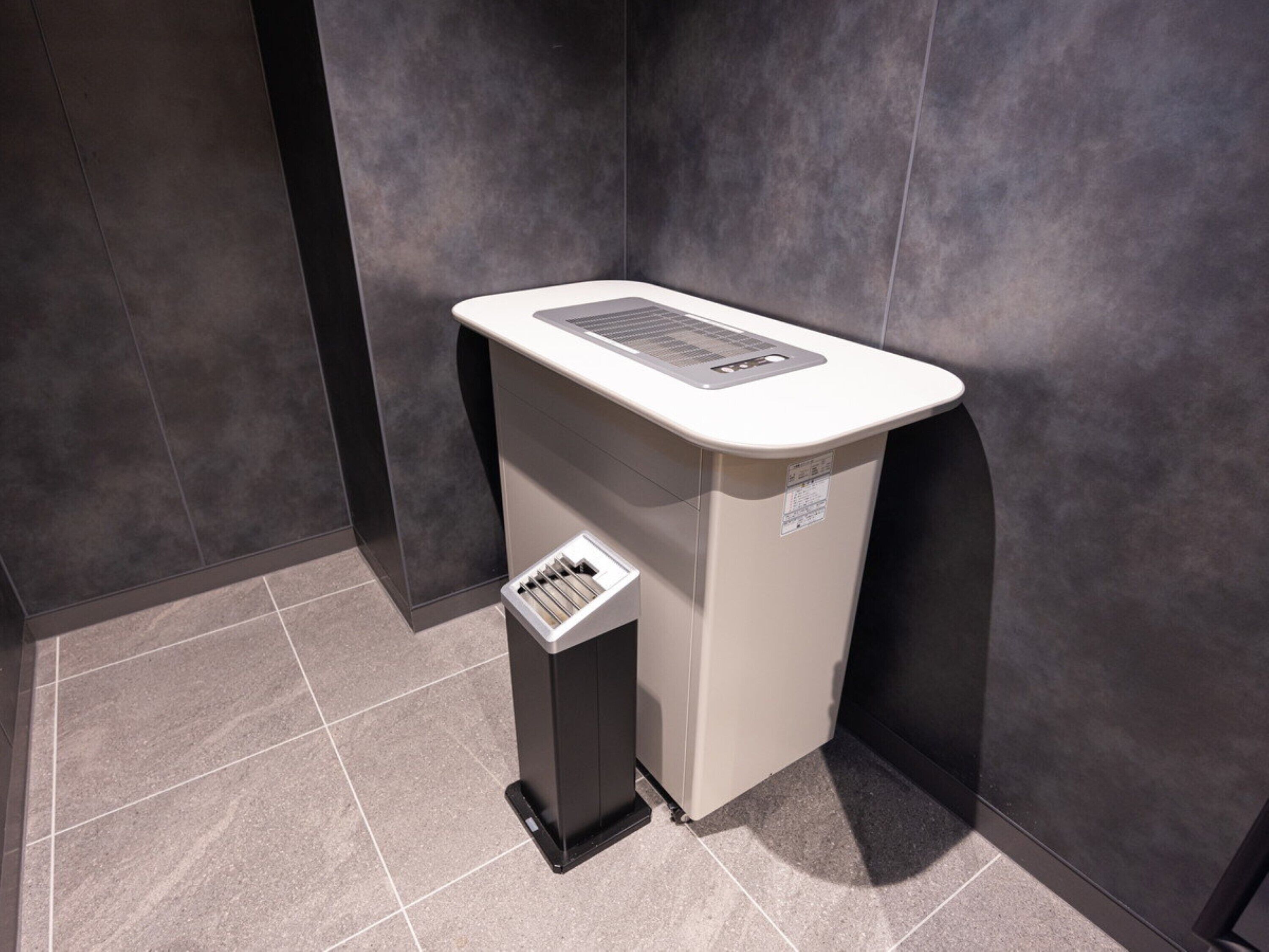 Une salle de bain moderne avec un lavabo blanc, une poubelle et des murs recouverts de carreaux foncés.