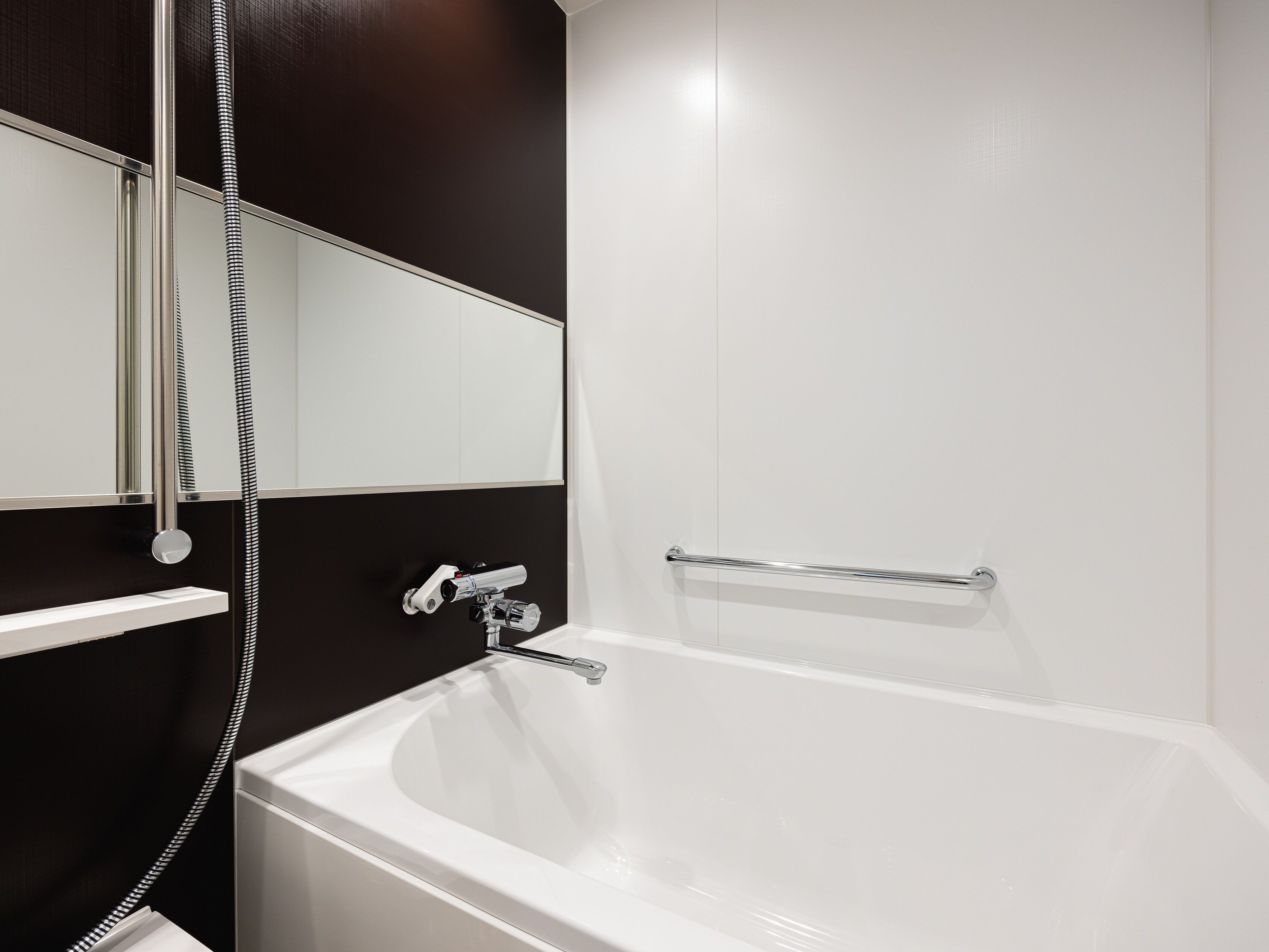 A modern bathroom with a white bathtub, a handheld showerhead, a wall-mounted mirror, and a towel rack.