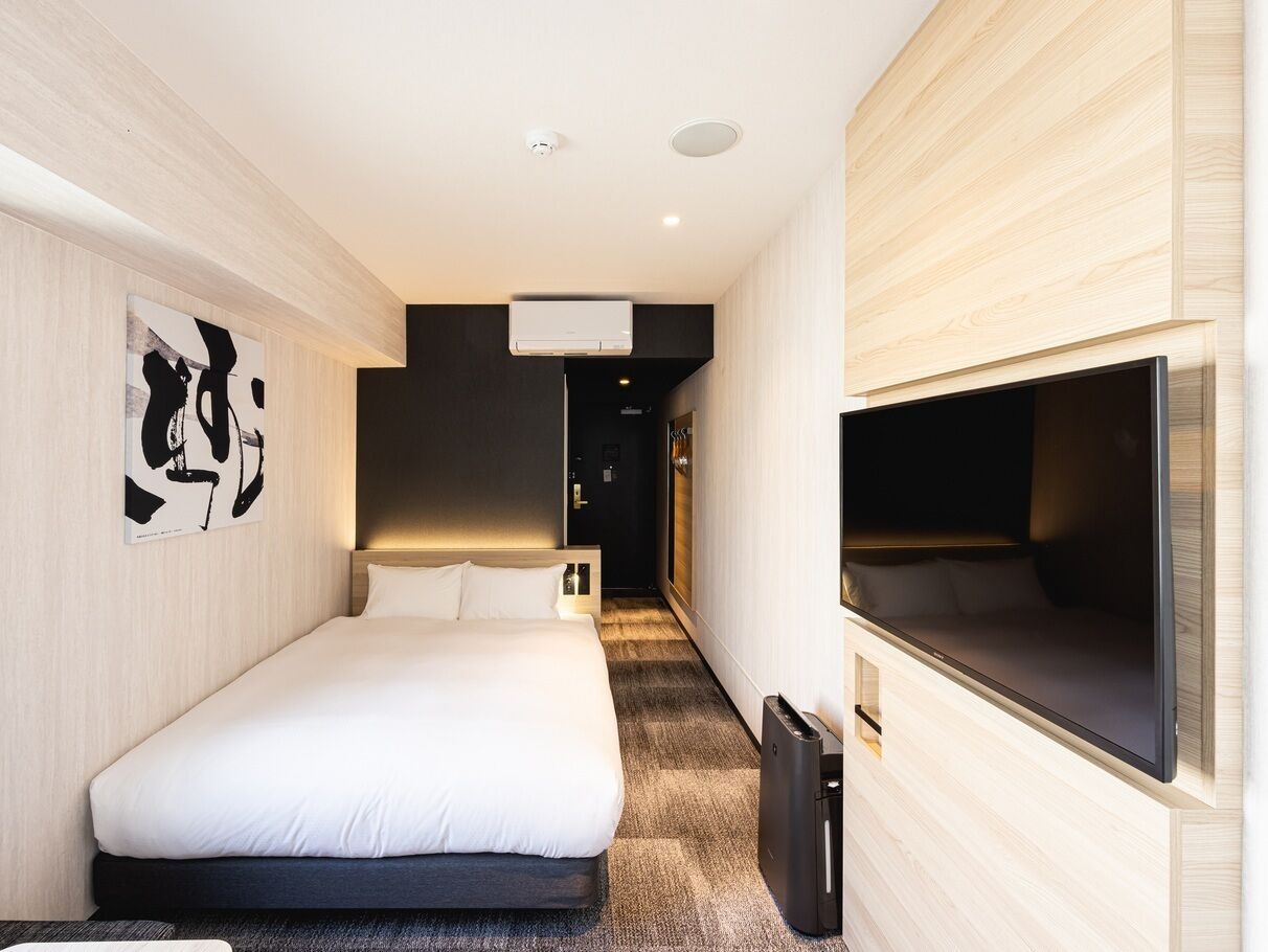 Quarto de hotel moderno com uma cama grande, televisão de tela plana e corredor que leva a um banheiro.