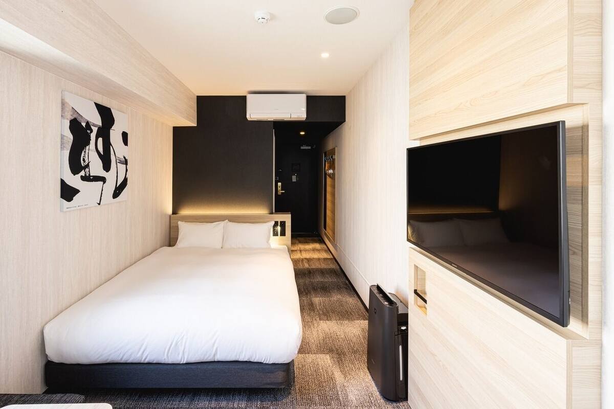 Una habitación de hotel moderna con una cama grande, un televisor de pantalla plana y un pasillo que conduce a un baño.