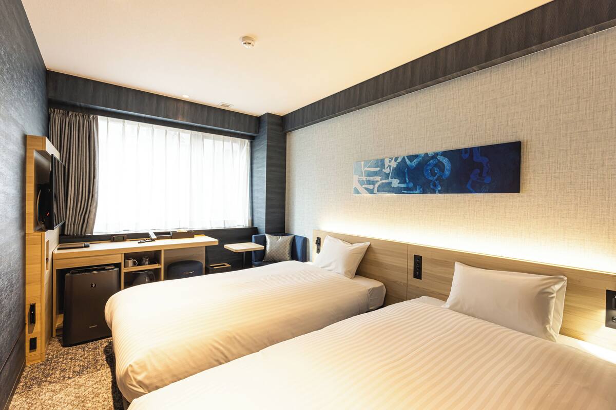 Habitación de hotel con dos camas, un escritorio, un televisor y una ventana con cortinas.