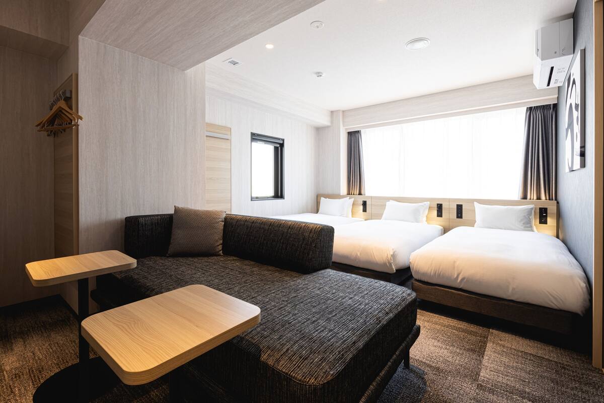 Una habitación de hotel moderna con un sofá, dos camas, una mesita y una ventana con cortinas.