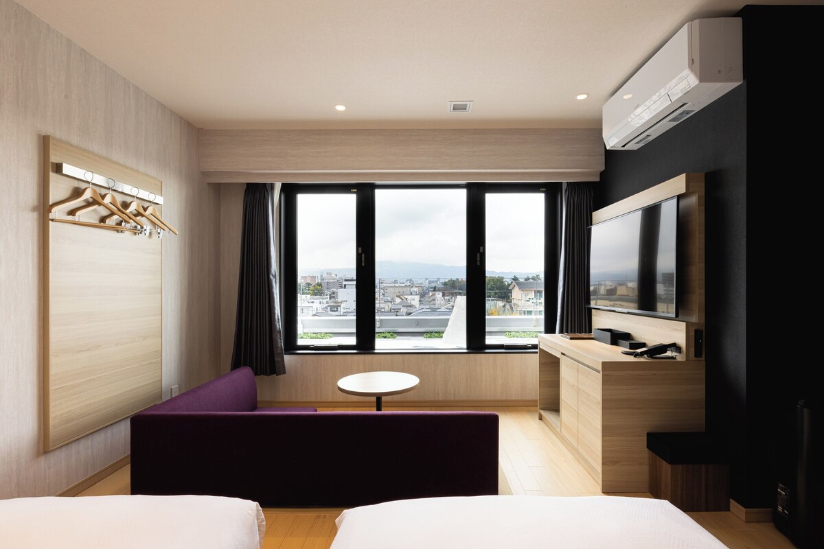 Habitación de hotel con cama, sofá, escritorio, televisor y ventana con vista a la ciudad.