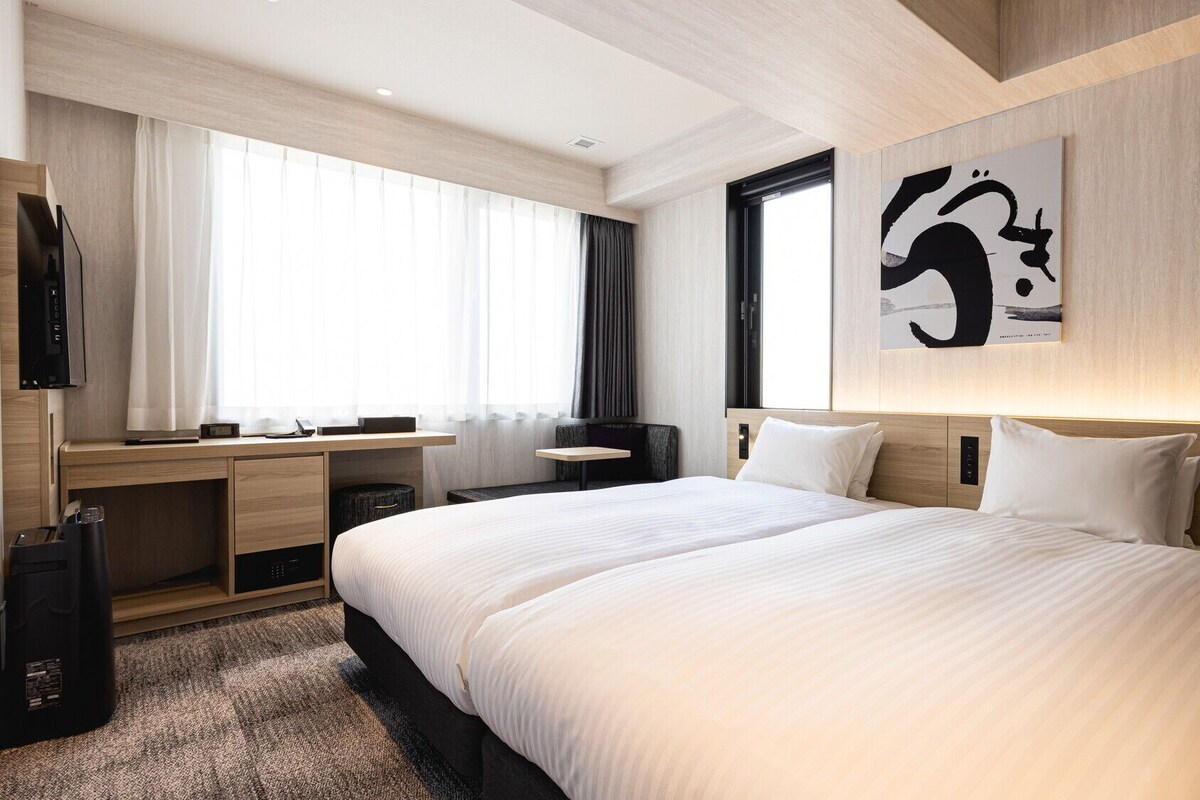 Habitación de hotel con una cama grande, un escritorio, una silla, un televisor y una obra de arte colgada en la pared.