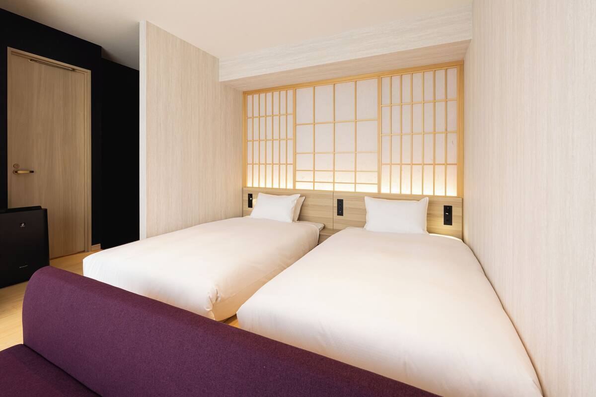 Habitación de hotel con dos camas, un sofá morado, un cabecero de madera y un armario negro.