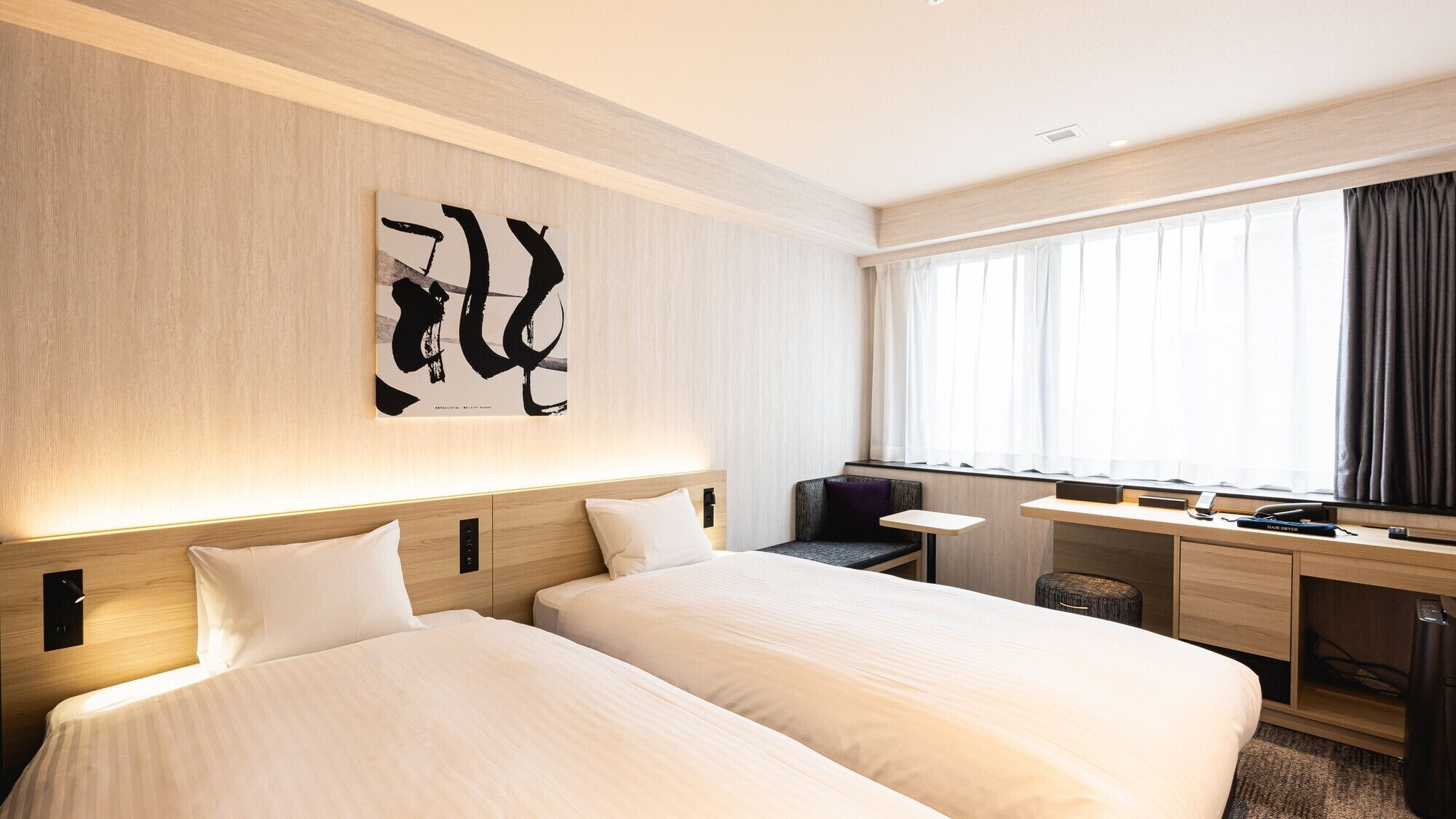 Quarto de hotel com duas camas, uma escrivaninha, uma cadeira, uma janela grande com cortinas e uma obra de arte na parede.