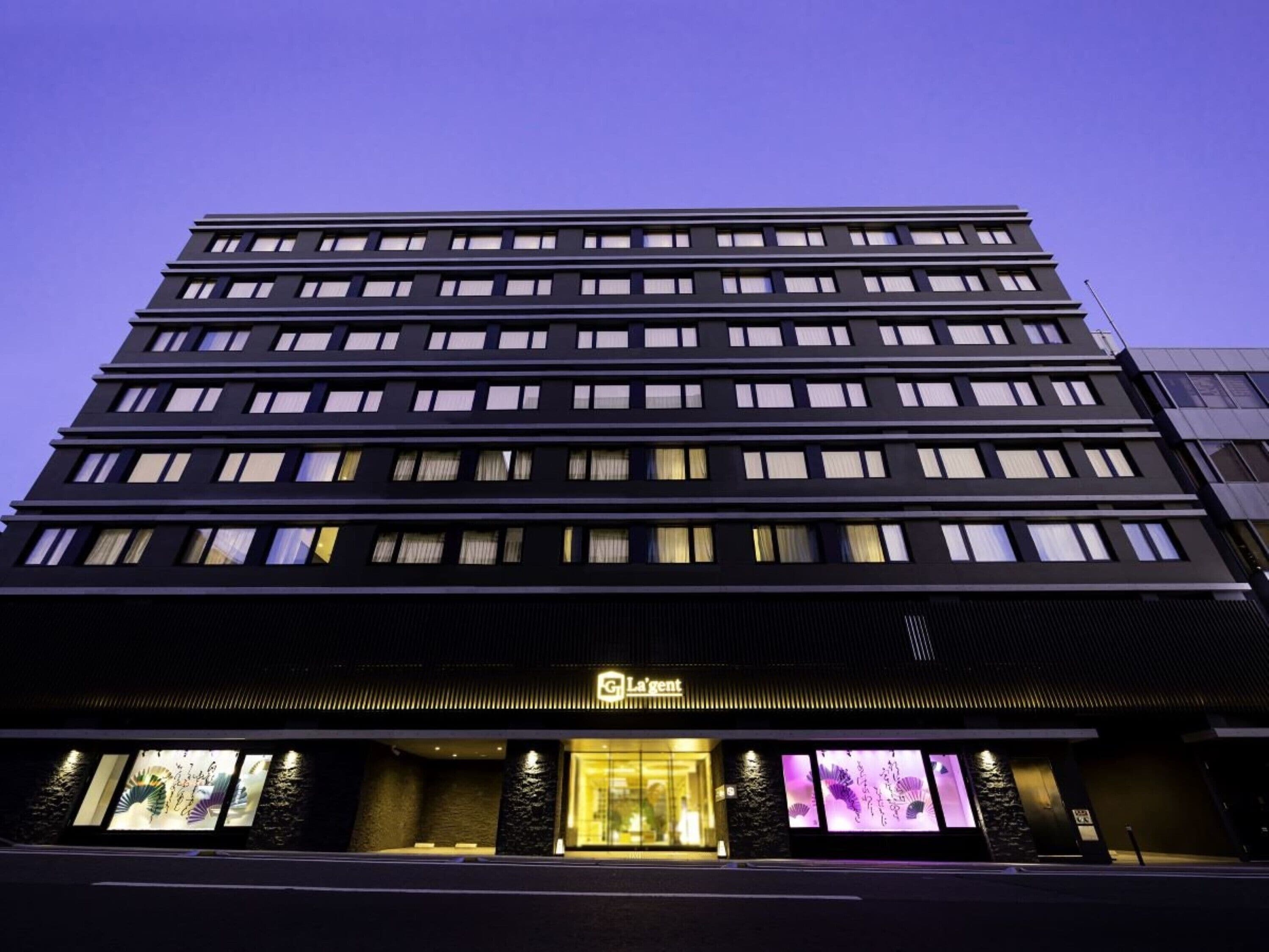 A multi-story hotel with a modern facade, illuminated windows, and a prominent entrance with a sign.