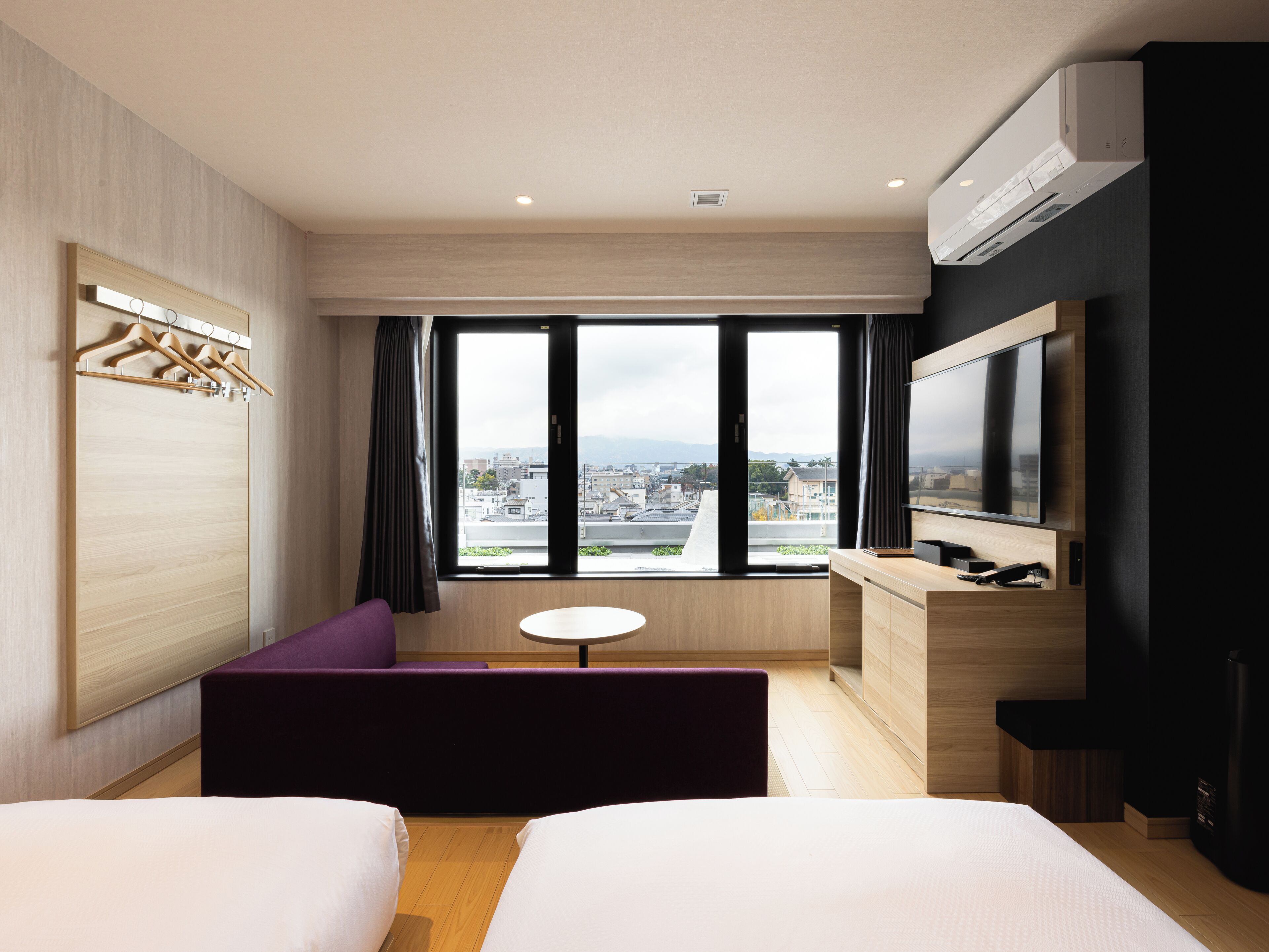 A modern hotel room with a large window, a flat-screen TV, a sofa, and a desk.