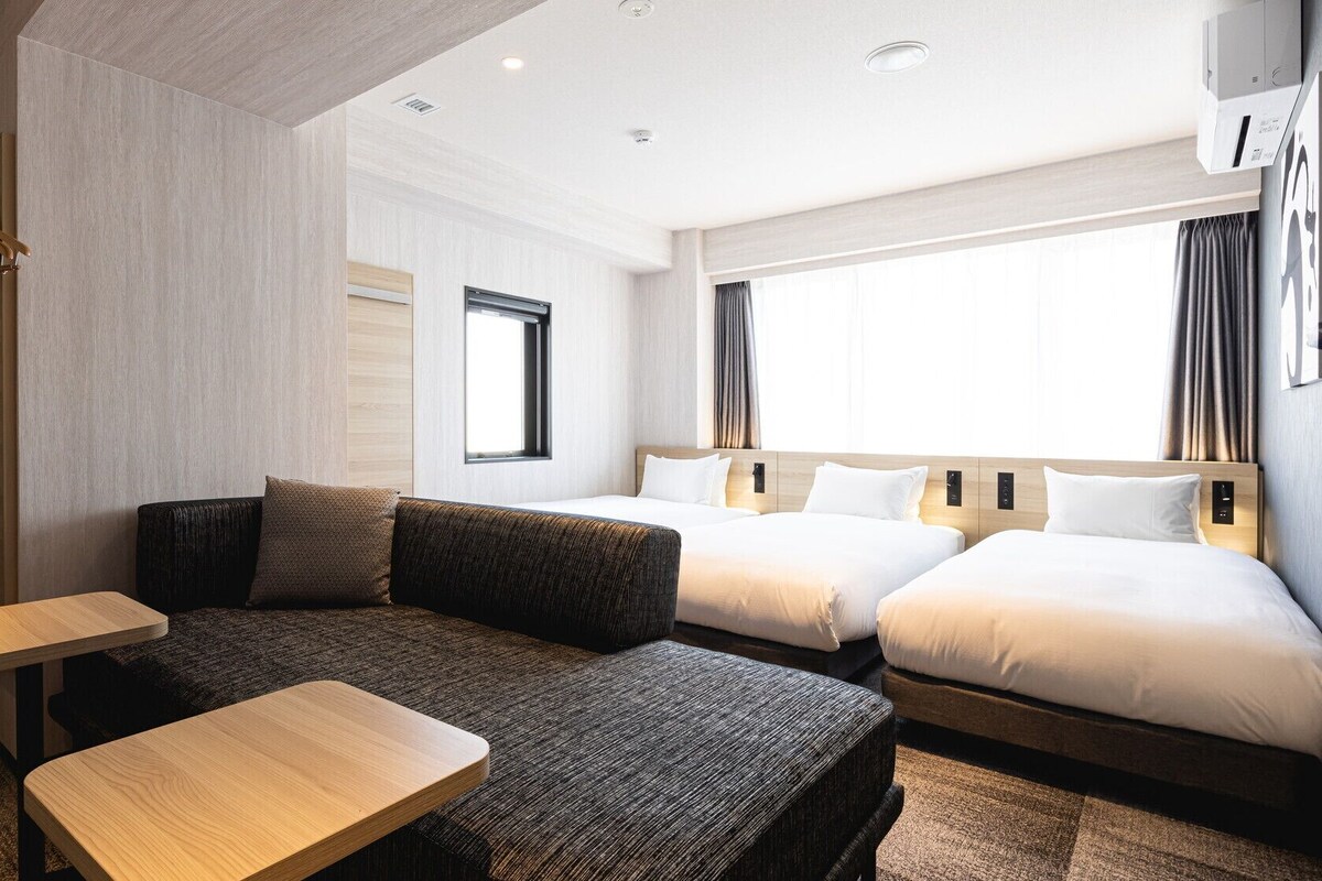 Una habitación de hotel con sofá, dos camas, una mesita y una ventana.