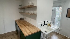 Cocina compacta con encimera de madera, un lavamanos integrado y estantes de madera arriba.