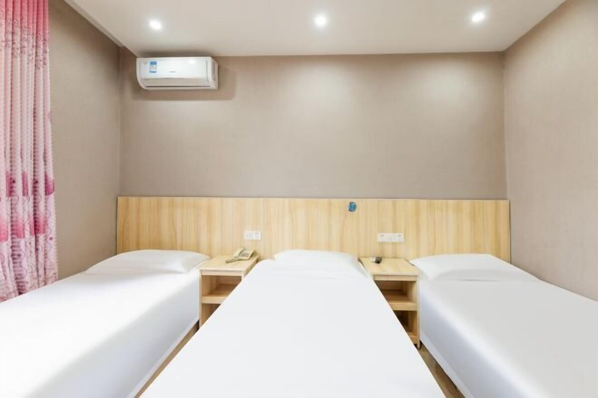 Quarto de hotel com duas camas de solteiro, cabeceira de madeira, ar condicionado fixado na parede e mesas de cabeceira com luminárias.
