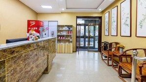 A reception area with a marble counter, wooden chairs, framed artwork on the walls, and a glass door leading outside. - More Joy Express Hotel (Dacheng)