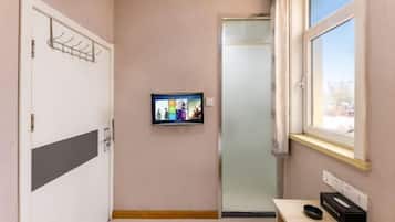 A room with a door, a coat rack, a television on the wall, a window, and a small table with a box and a remote.