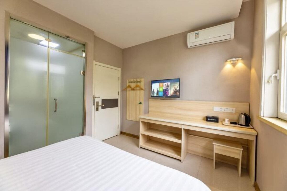 Quarto de hotel com cama, escrivaninha com cadeira, televisão e guarda-roupa.