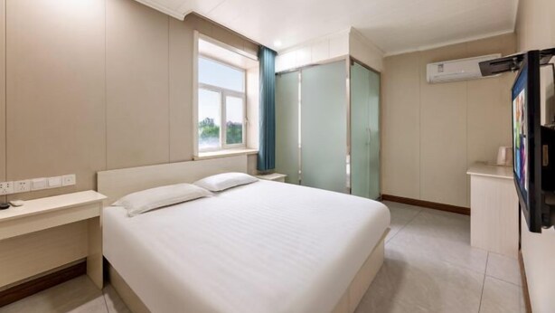A hotel room with a bed, bedside table, window, wardrobe, and a TV. - More Joy Express Hotel (Dacheng)