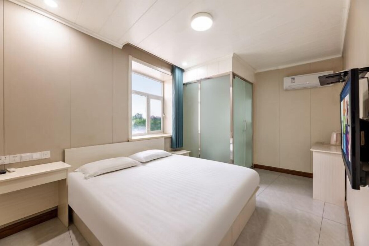 Quarto de hotel com cama, mesa de cabeceira, janela, guarda-roupa e televisão.