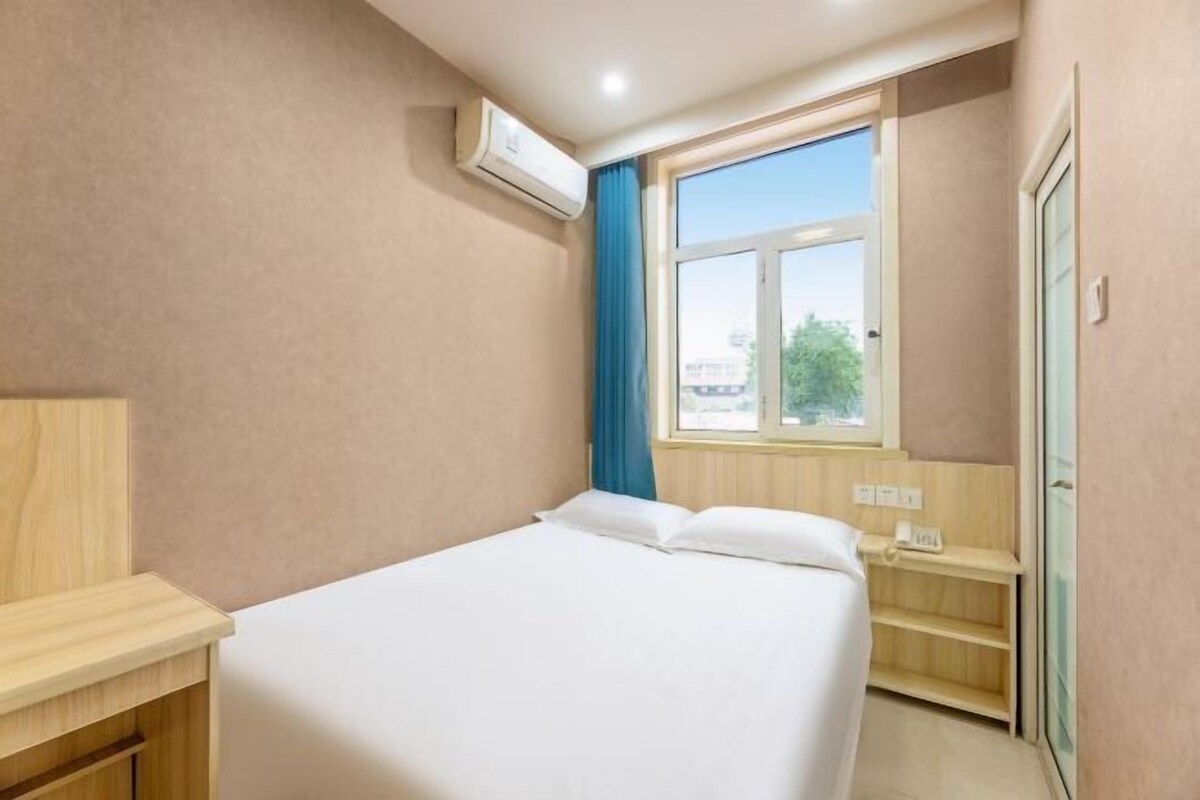 Quarto de hotel com cama, escrivaninha, janela com cortinas e ar condicionado.