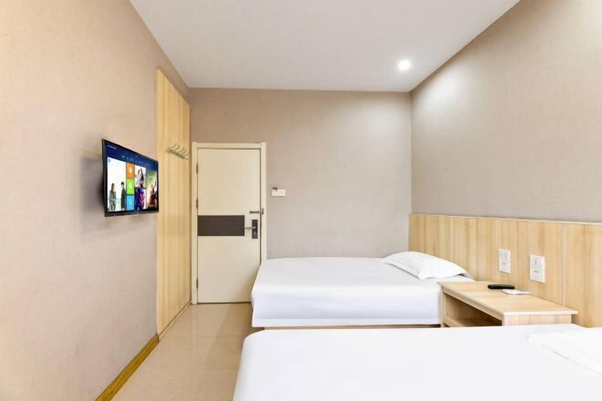 A hotel room with two beds, a TV mounted on the wall, and a wooden headboard.