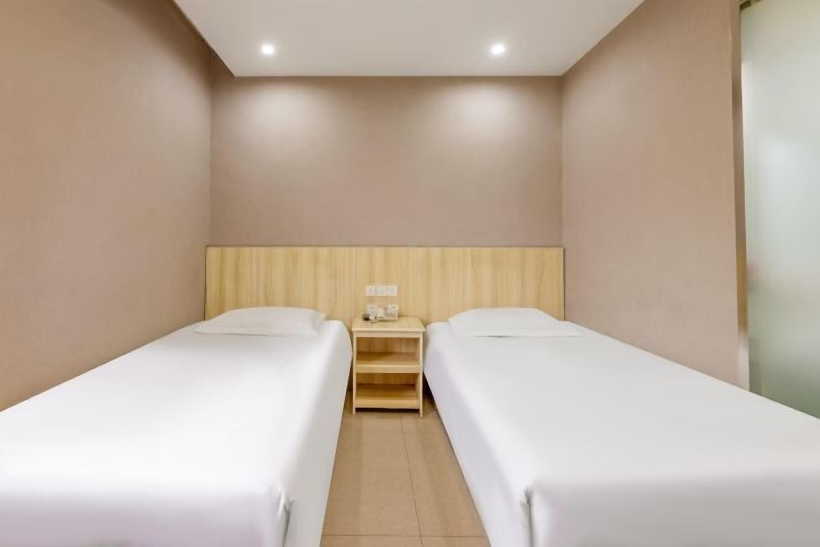 Habitación doble con dos camas individuales, cabecera de madera, mesita de noche con lámpara y una pequeña mesa.